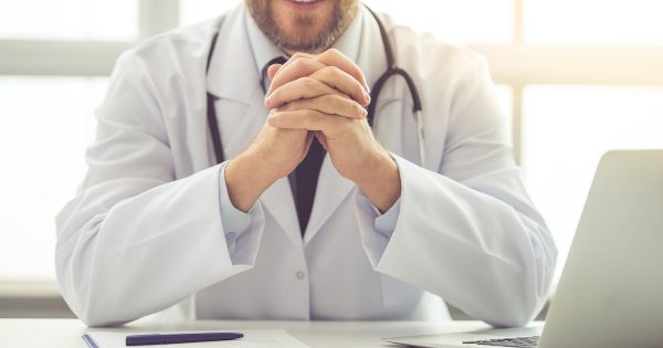Cropped image of handsome medical doctor in white coat smiling while sitting in his office