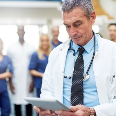 Doctor at hospital looking at tablet. Medical team standing in background.